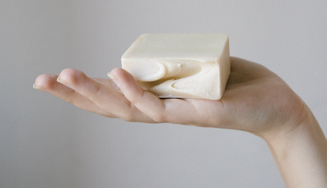 A close-up of a person's hand holding a bar of goat's milk soap.